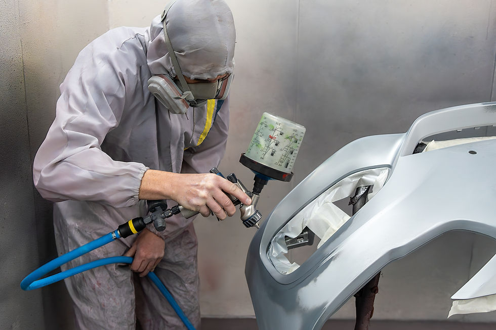 Skilled mechanic in protective gear expertly applies paint to a car's surface in a well-ve