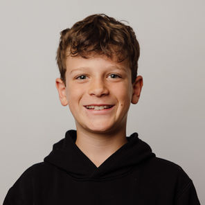 boy swearing black sweat shirt with brown curly hair smiling at the camera.