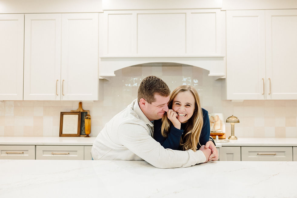 a young couple in their brand new kitchen leaning on counter tops touching shoulders smiling looking at camera and man is hugging his wife
