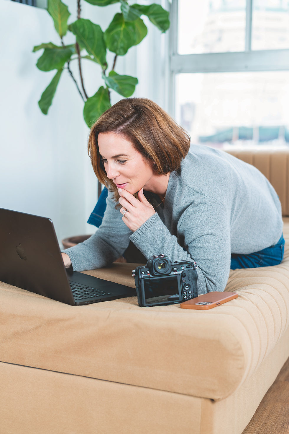 Woman laying on chaise lounge looking at laptop with camera nearby