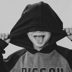 Boy looking at camera in solid background and black and white image covering face with sweatshirt sticking out tongue