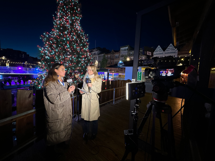 Two reporters from local TV station Notts TV, stood on a balcony that overlooks a large christmas tree, waiting to go live on air from Nottingham's Winter Wonderland.