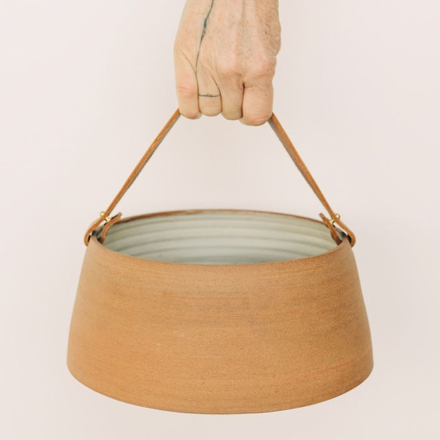 Hand houdt bruine keramische mand met leren handvat