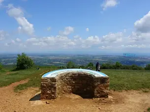 Abri en pierre avec toit bleu sur un belvédère, vue panoramique sur la vallée sous un ciel bleu nuageux, quelques promeneurs.