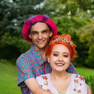 Wedding couple in bold, colorful outfits smiling at their wedding at Ash Barton Estate, North Devon, surrounded by lush greenery.