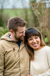 Couple smiling and laughing together outdoors with a soft countryside background.