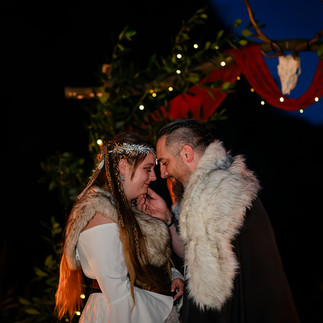 Bride and groom in Viking-themed attire sharing a tender moment under fairy lights at Carwinion House during an evening wedding celebration