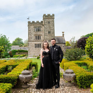 Bride and Groom both in Black formal wear with Pengersick Castle in the Background on their wedding day