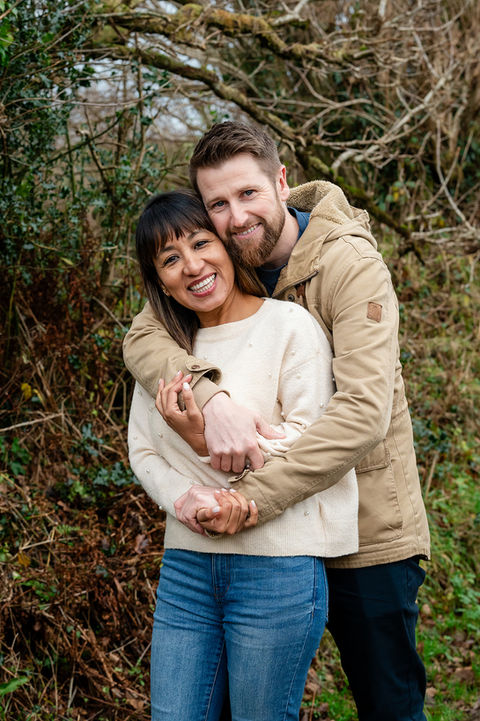 Happy couple embracing in a woodland area, with vibrant greenery and a natural outdoor setting.