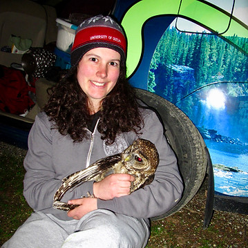Staff member Jasmine holding an adult spotted owl and smiling.