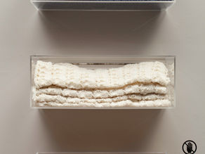 Three knitted throws folded on clear shelves, coloured blue, cream, and yellow, hanging above one another on a wall.
