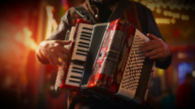 Close-up of a musician playing a red piano accordion with button keys, performing under warm stage lights at a festive indoor event.