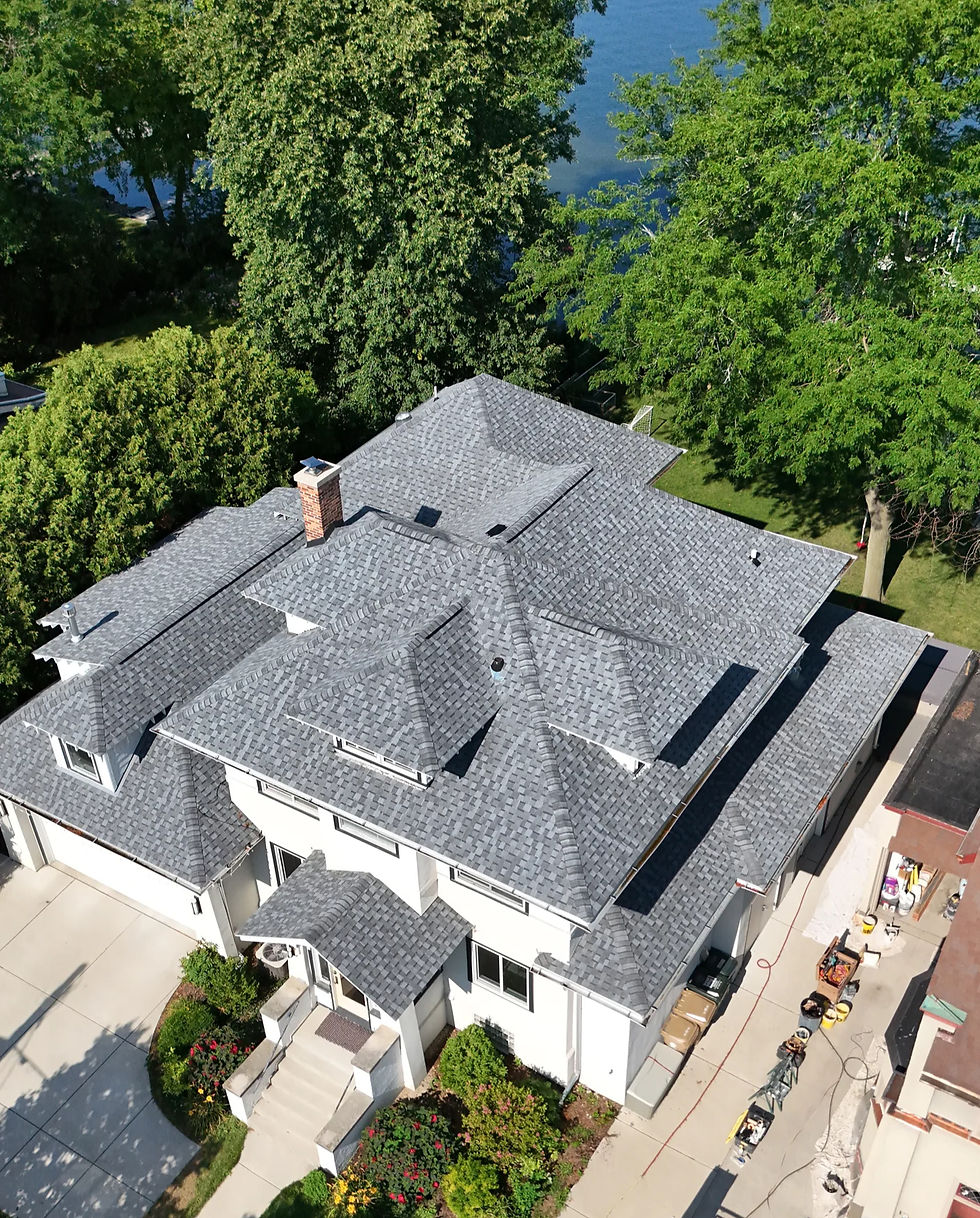 Pewter-colored asphalt shingle roof installed on a white house with the water of Lake Mendota in Madison, WI visible in the background.
