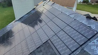 Progress shot of a residential roof in Madison, WI, showing newly installed black solar shingles over water-shield underlayment during a roofing project.