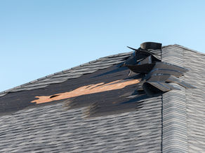 asphalt shingles on residential roof damaged after a wind storm against a blue sky