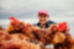 A woman wearing a red hat and rubber gloves holds a string of red seaweed