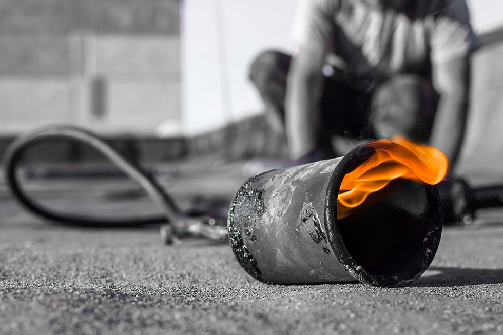 Eine Person bringt bei bewölktem Himmel mit einem Schweißbrenner eine Rolle Dachmaterial auf einem Flachdach an. Im Hintergrund sind weitere Rollen und Geräte zu sehen.