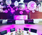Hochzeitslocation mit Sicht auf DJ, Tanzfläche und luxuriösem Tischgedeck. von der Decke hängen riesige Ballons die mit Magenta farbenem Licht angestrahlt werden