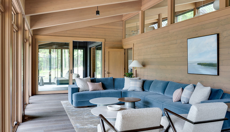 Light-filled living room with an organically curved blue sectional, white bouclé chairs, Douglas fir walls and tailored plaid pillows