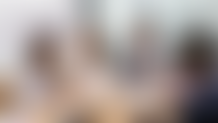 Ein Projektteam sitzt zusammen am Tisch. Eine Frau, die Auftraggeberin, brieft das Team für einen Teamevent.