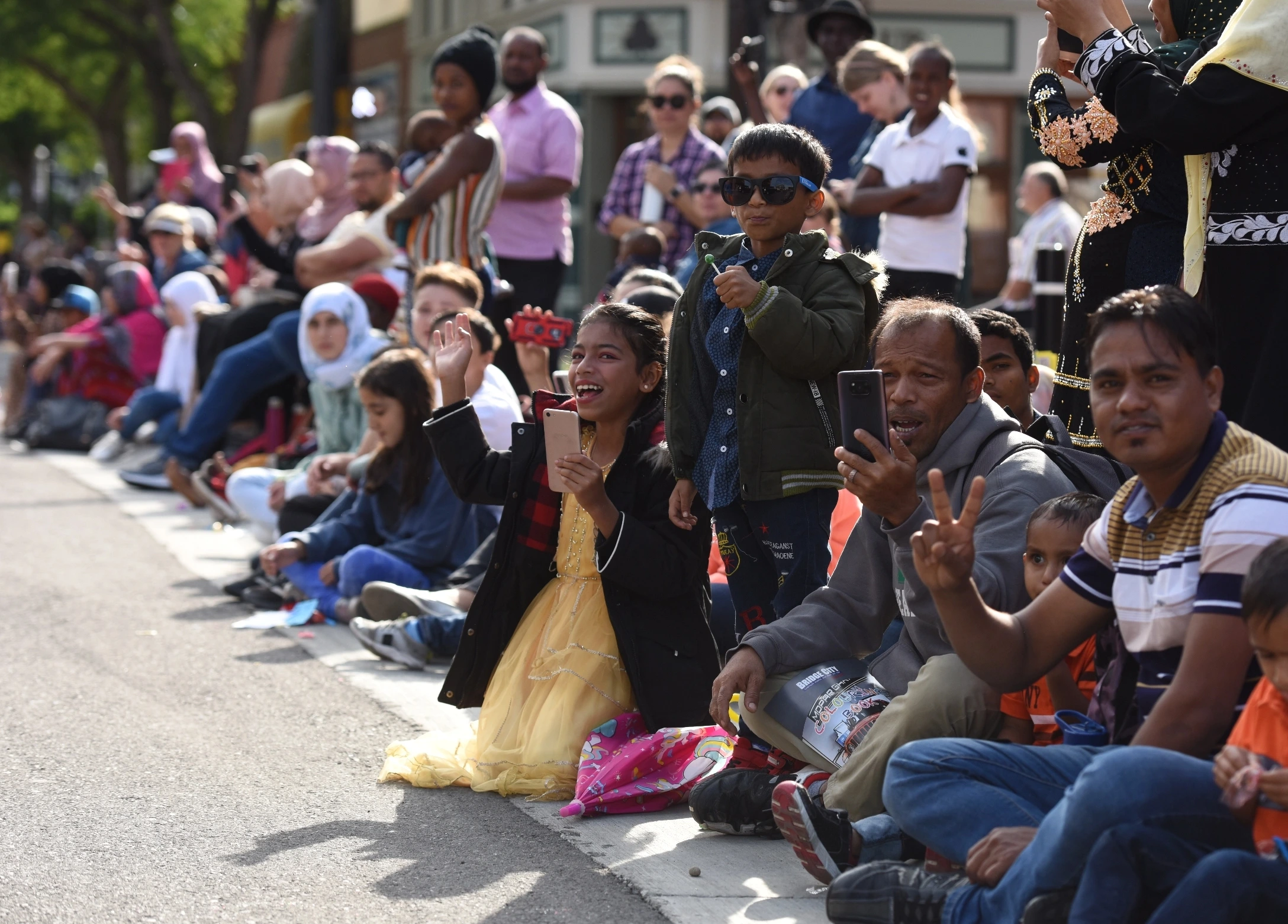 group of people sitting on a street curb at a parade