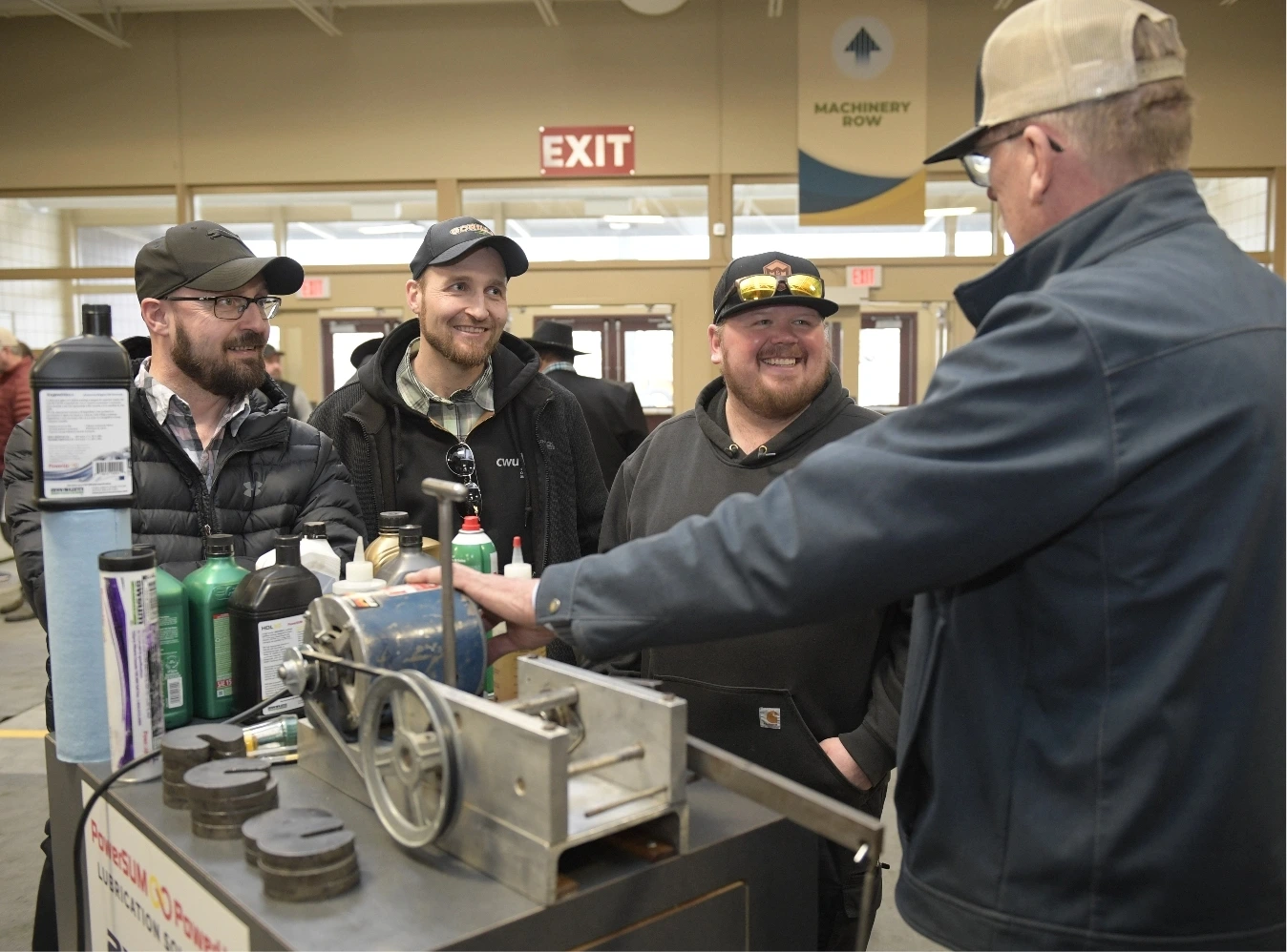 4 men standing at a booth at an agricultural trade show getting a demostration
