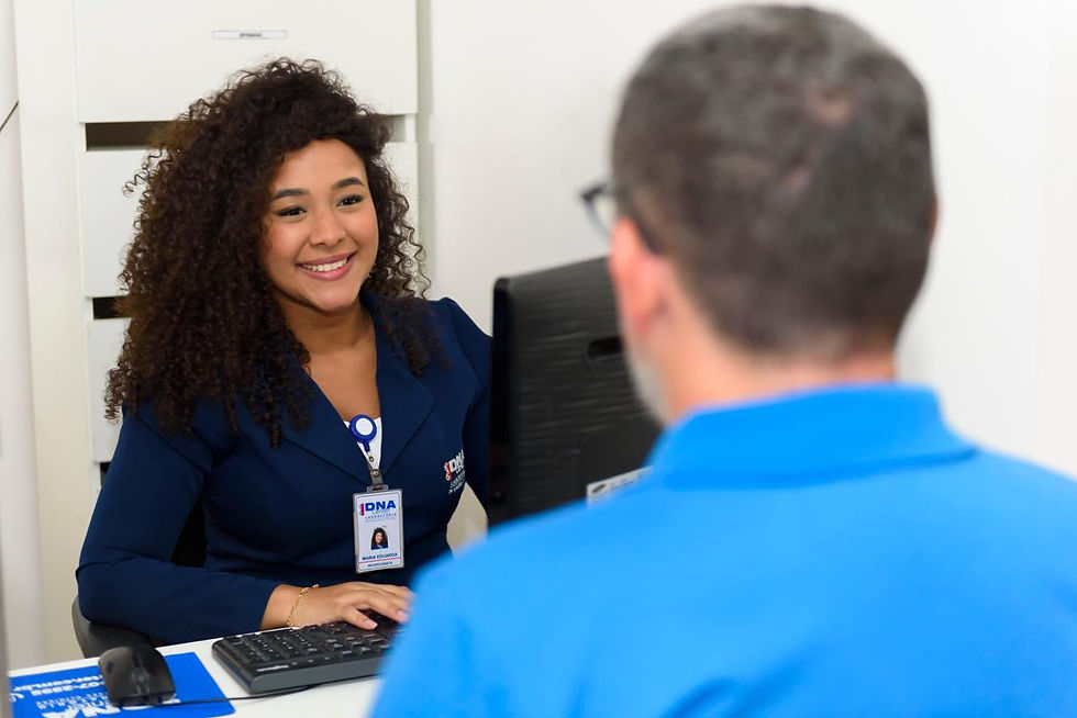 Atendente do DNA Center recebe paciente em balcão de atendimento, sorrindo enquanto utiliza o computador.
