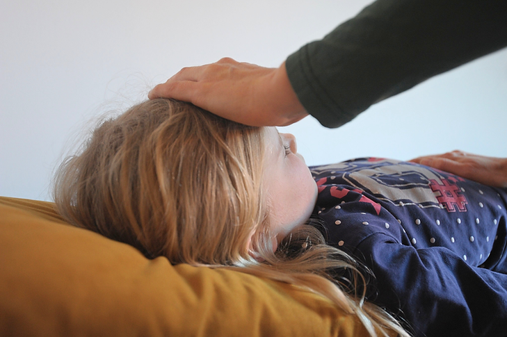 Therapeutin legt Hand auf Stirn eines Kindes während energetische Behandlung