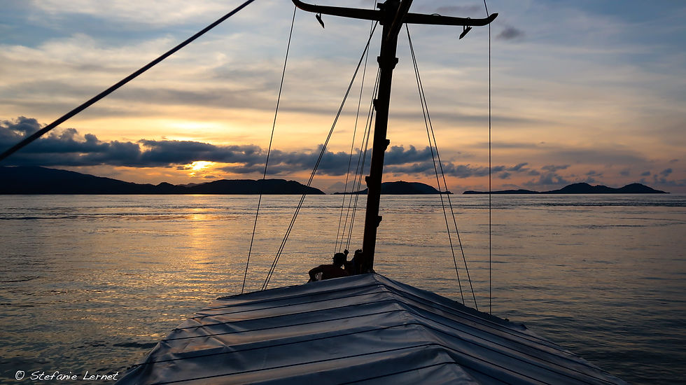 Boat deck at sunset with silhouetted figures against a calm sea. Text: © Stefanie Lernet. The sky glows in warm orange hues.