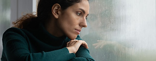 Thoughtful stressed young hispanic latin woman sitting on windowsill, looking outside on r