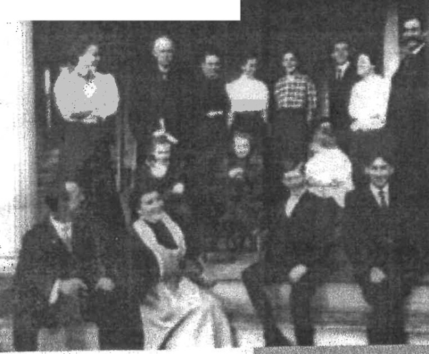 Black-and-white photo with 15 people posed on a front porch and its steps. 