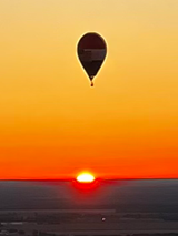 Hot air balloon silhouette above orange sunrise