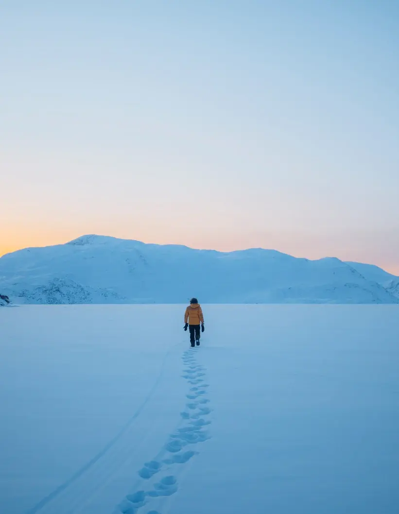 Traveller walking across snow toward distant mountains at dusk