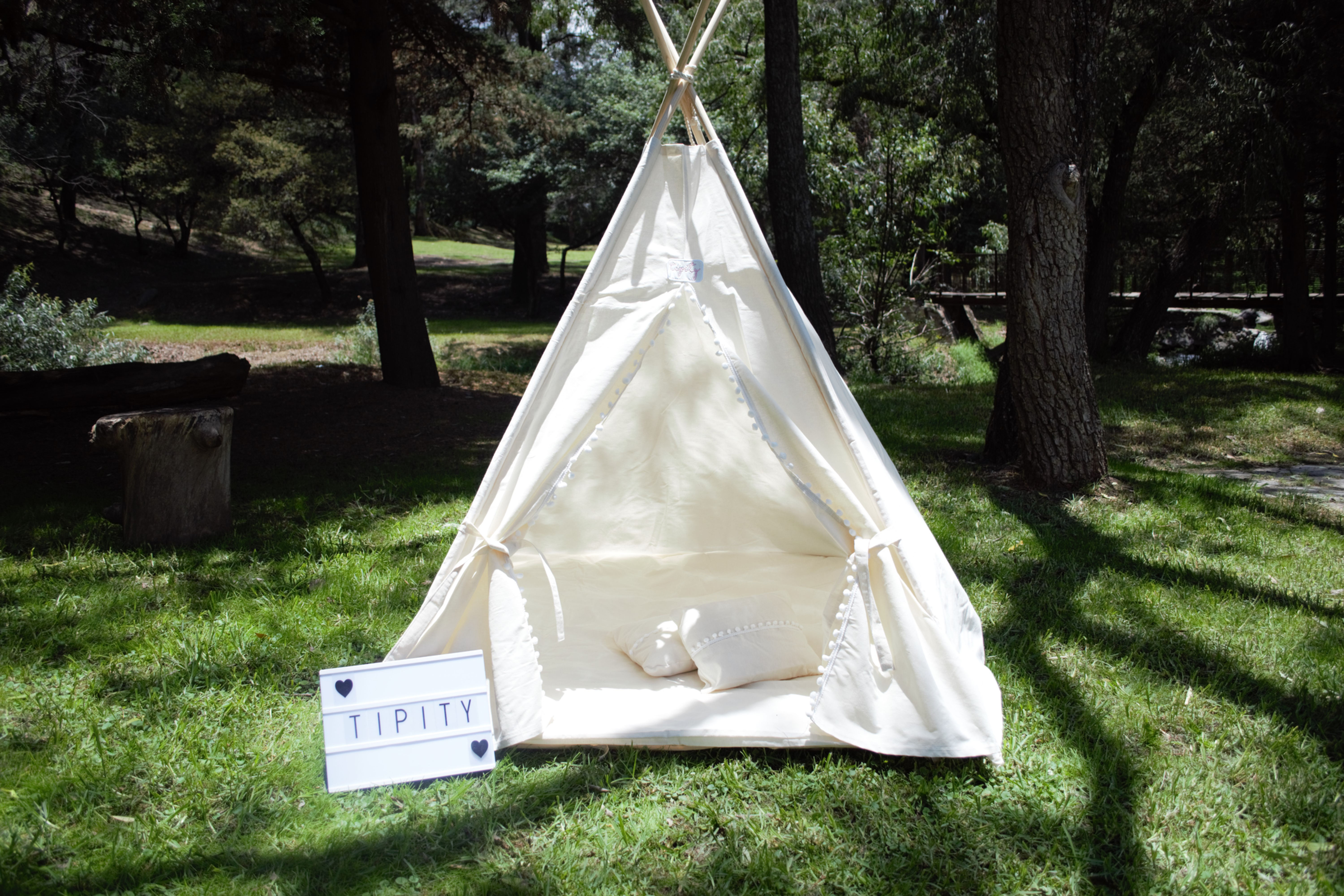 Tipity Tipi tent on green grass with Tipity sign and puff de tela.