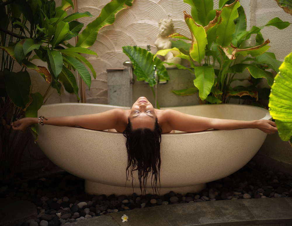 Woman in bathtub surrounded by tropical plants.