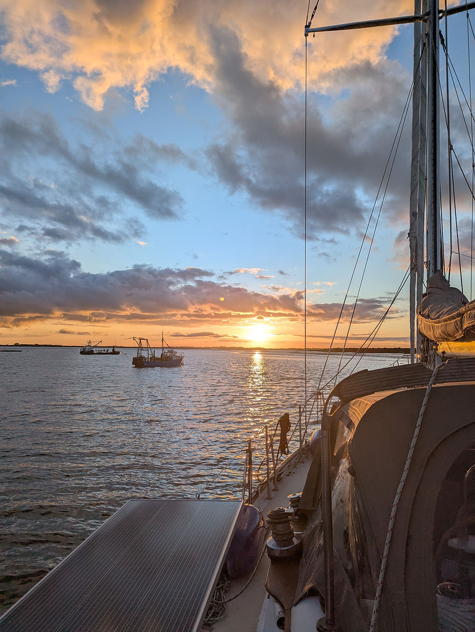 Boat deck at sunset on calm water with two ships in the distance. Vibrant orange and blue sky with dramatic clouds. Peaceful mood.
