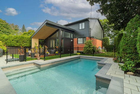 Piscine moderne intégrée à une cour arrière avec maison à toit incliné et bardage contemporain.