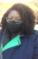 Courtney wearing a blue and green trench with a gray scarf, glasses, and a black mask gazing into the camera.