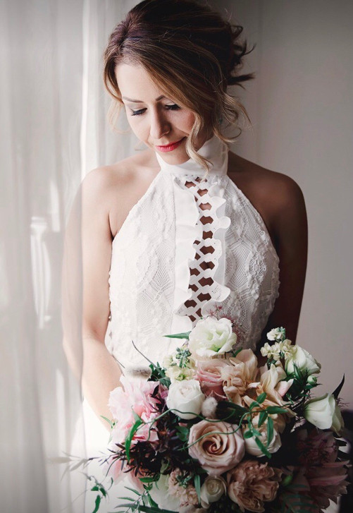 bride standing by window holding bouquet of flowers