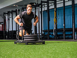 Hombre empujando trineo sobre césped artificial Grasspro Gym Turf