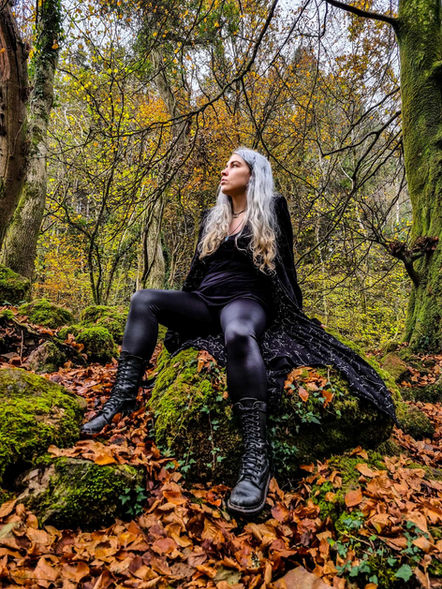 girl with grey hair wearing all black, sitting in an autumnal forest