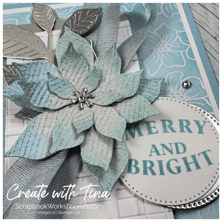 Close-up of a blue shimmering poinsettia with silver foil leaves and a Merry and Bright sentiment.