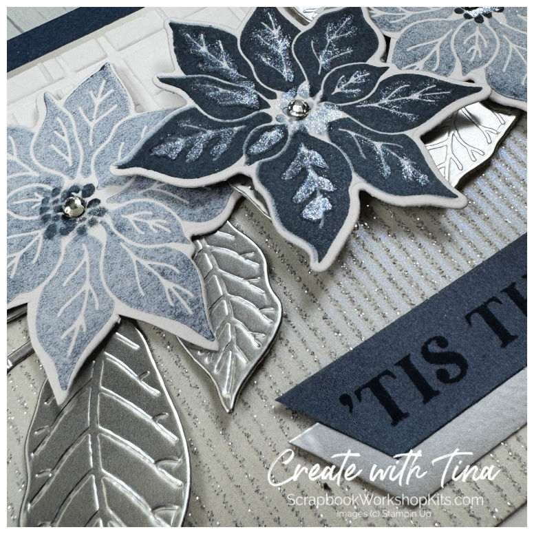 Close-up of navy and pale blue poinsettias layered with silver foil leaves and shimmering specialty paper.