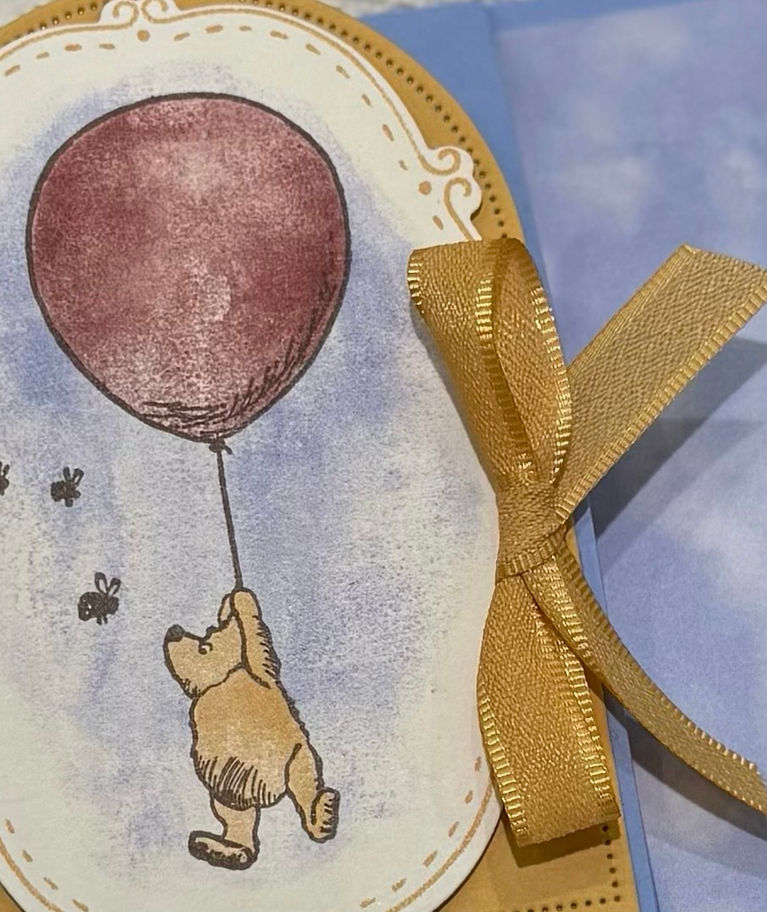 Close-up handmade Winnie the Pooh card featuring Pooh floating with a balloon, soft blended background, and gold ribbon