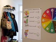 Flur mit Kinder-Garderobe und farbigem Morgenplan Emmas Morgenritual neben bunter rainbowatch Lernuhr als echte WandUhr.