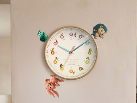 Mutter und Kind am Tisch, sie reden und schreiben. An der Wand eine rainbowatch Lernuhr. Auf ihrem Rahmen Rahmen rennen Hase, Igel und Schnecke einen Marathon. Helle, gemütliche Wohnzimmereinrichtung.