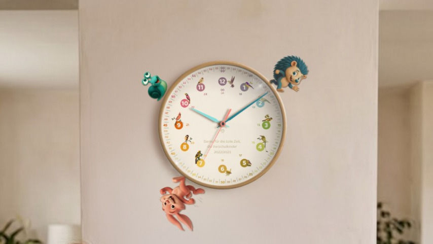 Bunte Wanduhr an heller Wand - mit den rainbowatch Lernzeiger- Characteren des Kinderbuchs Minu, Seki und Stundi; Zeiger zeigen kurz nach 10 Uhr, ruhige Innenraumstimmung.