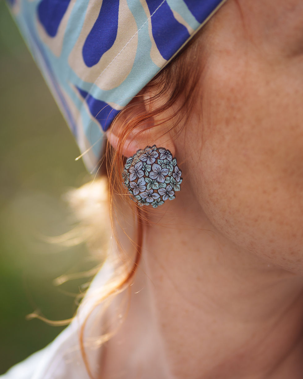 une boucle d'oreille fleurs hortensia bleu parme accrochée à l'oreille