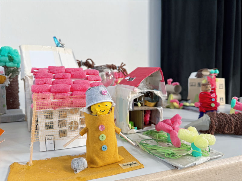 Auf einem Tisch stehen kleine Modelle von Figuren und Häusern, aus unterschiedlichen Materialien von - offenbar - Kinder- und Jugendhänden gestaltet.