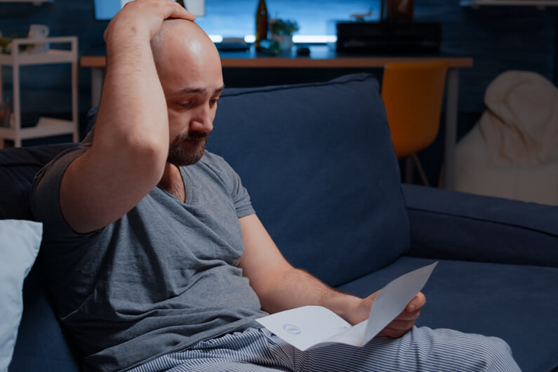 Ein Mann sitzt auf der Couch und sieht verzweifelt auf einen Brief